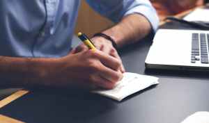 Man writing on a piece of paper at his desk while sitting