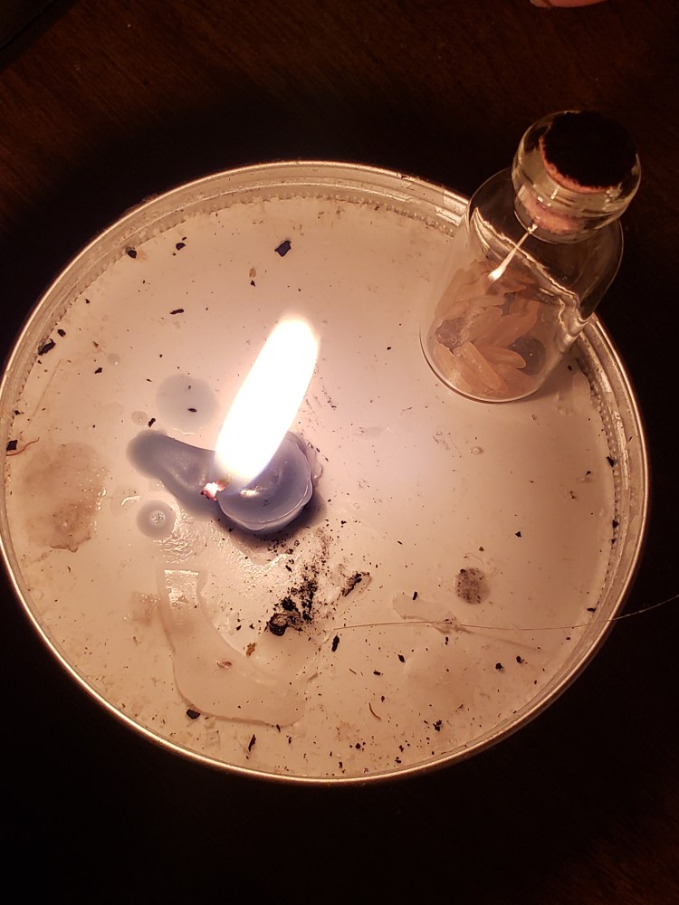 A candle burns beside a jar of rice and pepper corn